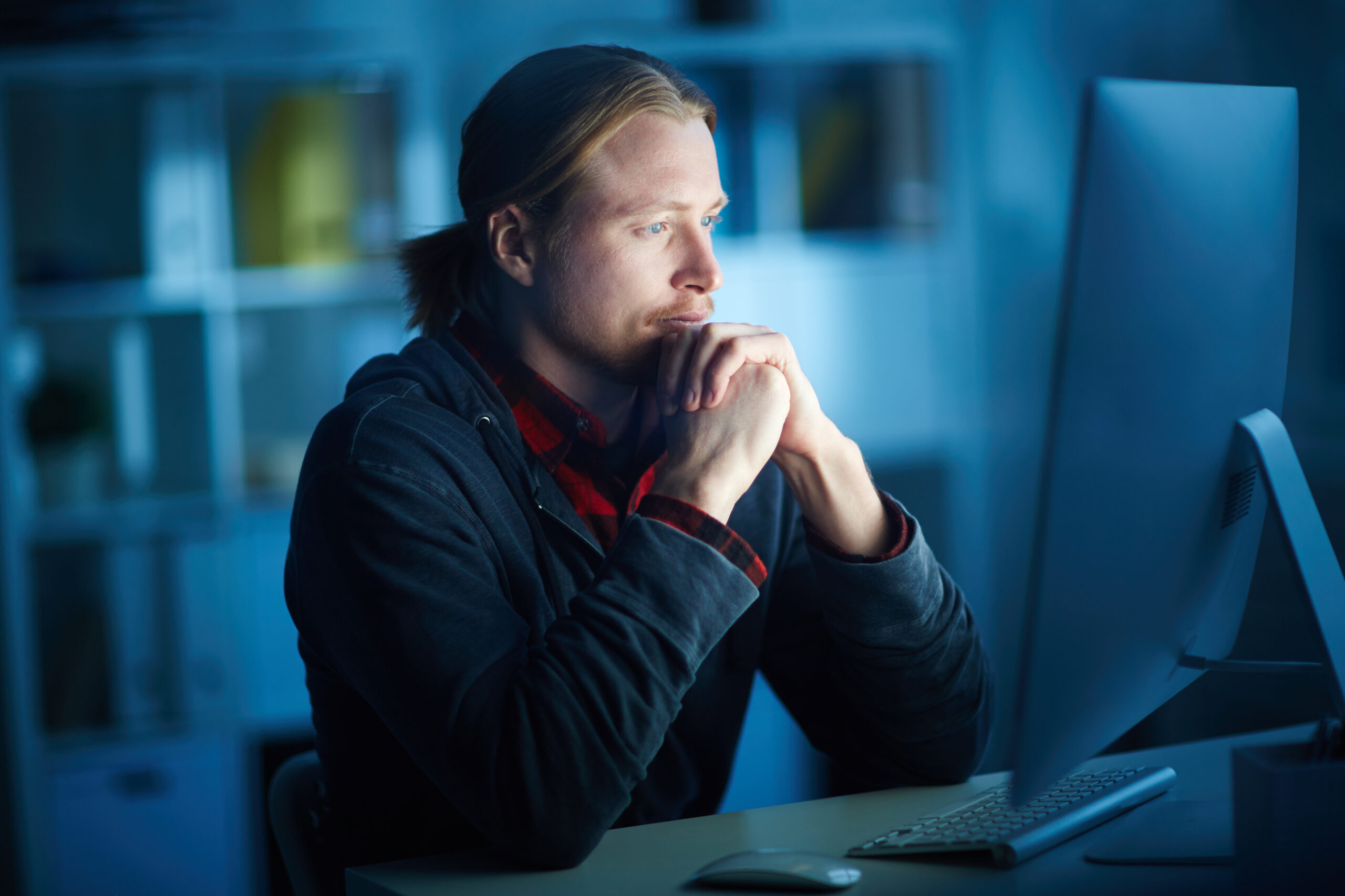 Serious man looking at a computer screen, in a dark office